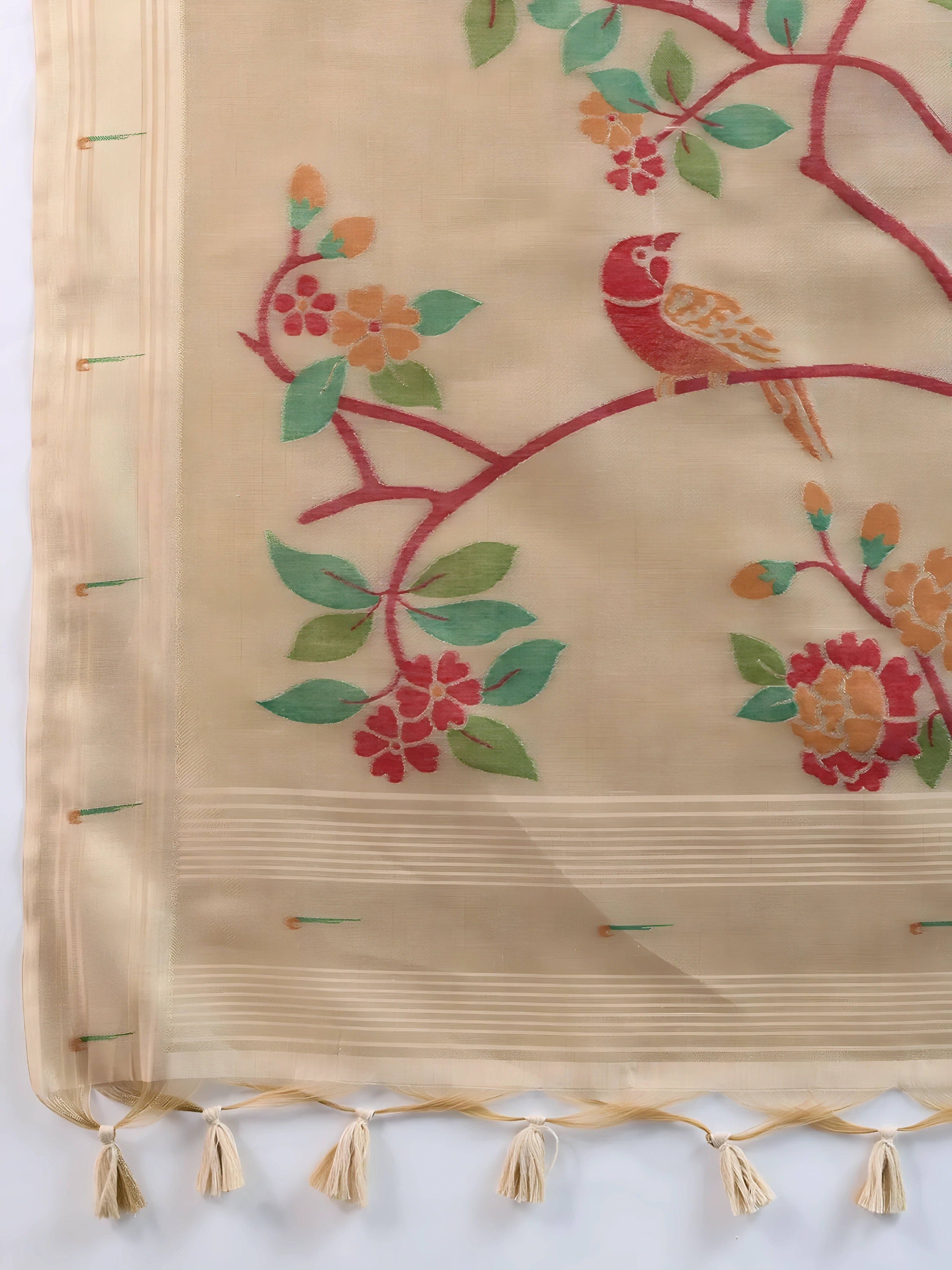  Woman wearing an elegant beige silk saree featuring delicate floral motifs and a hand-painted pallu, paired with a sleeveless red blouse and traditional jewelry, gracefully posing in a modern studio with olive green walls and patterned window light.
