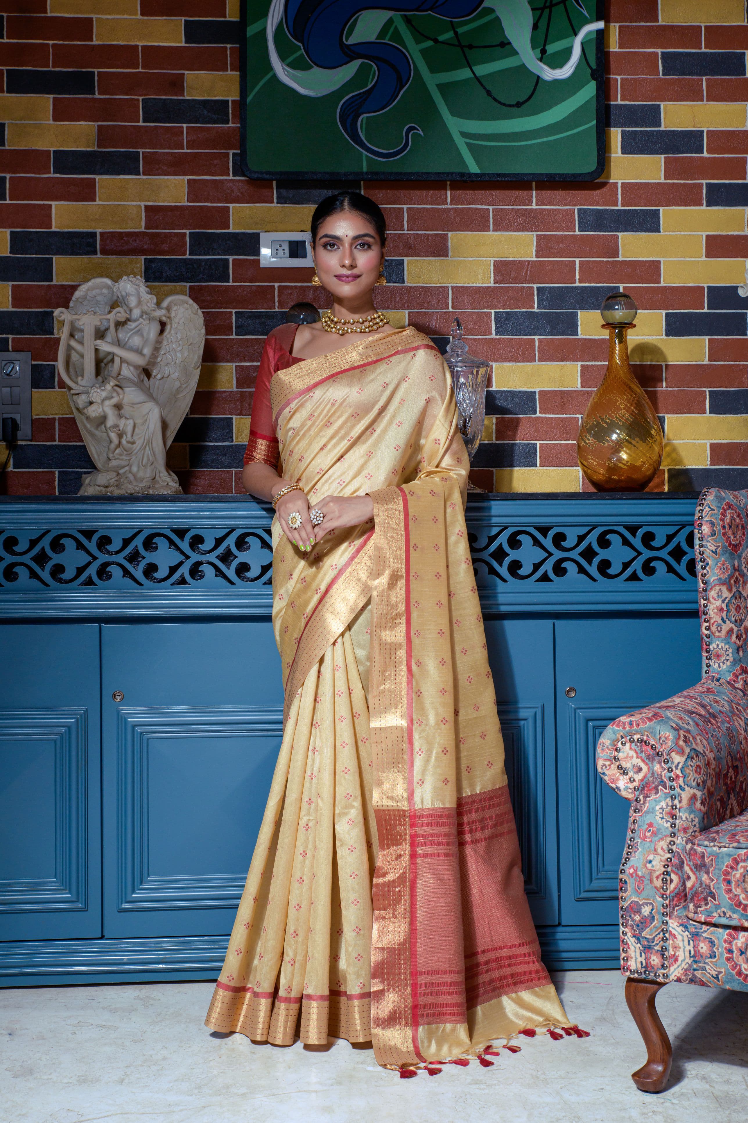 Beige saree with zari work and red border indoors