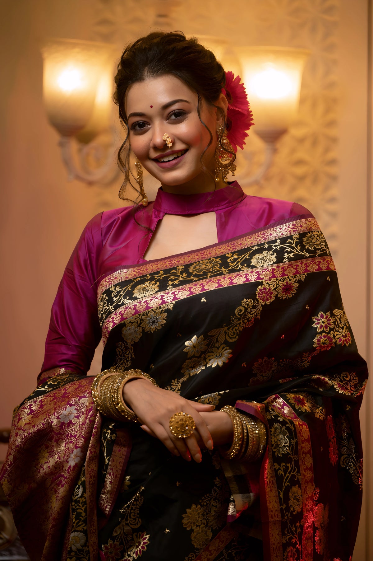A woman models a luxurious Black Soft Banarasi Silk Saree. The saree features dense, multi-colored Zari weaving of gold and pink florals, and a wide pallu with heavy gold and Fuchsia Pink accents. She wears a high-neck magenta blouse and gold jewelry, posing in a dramatically lit antique setting.