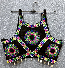 Black blouse featuring vibrant circular and oval mirror work with traditional Kutch multicolor embroidery, adorned with bold geometric borders and shell tassel drops along the hem. Displayed on a hanger against a textured silver background, highlighting its festive and culturally inspired ethnic design.