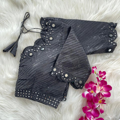 Black bridal blouse with scallop sleeves, featuring circular mirror work along the neckline, sleeves, and hem, sequin detailing throughout, and tie-up tassels, displayed on a textured grey and white fur background with a small potted plant nearby.