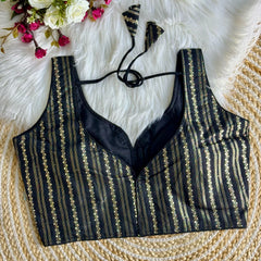 Black blouse top with intricate zari work design, featuring vertical stripes and floral patterns, displayed on a white fur background with a bouquet of white and pink flowers.