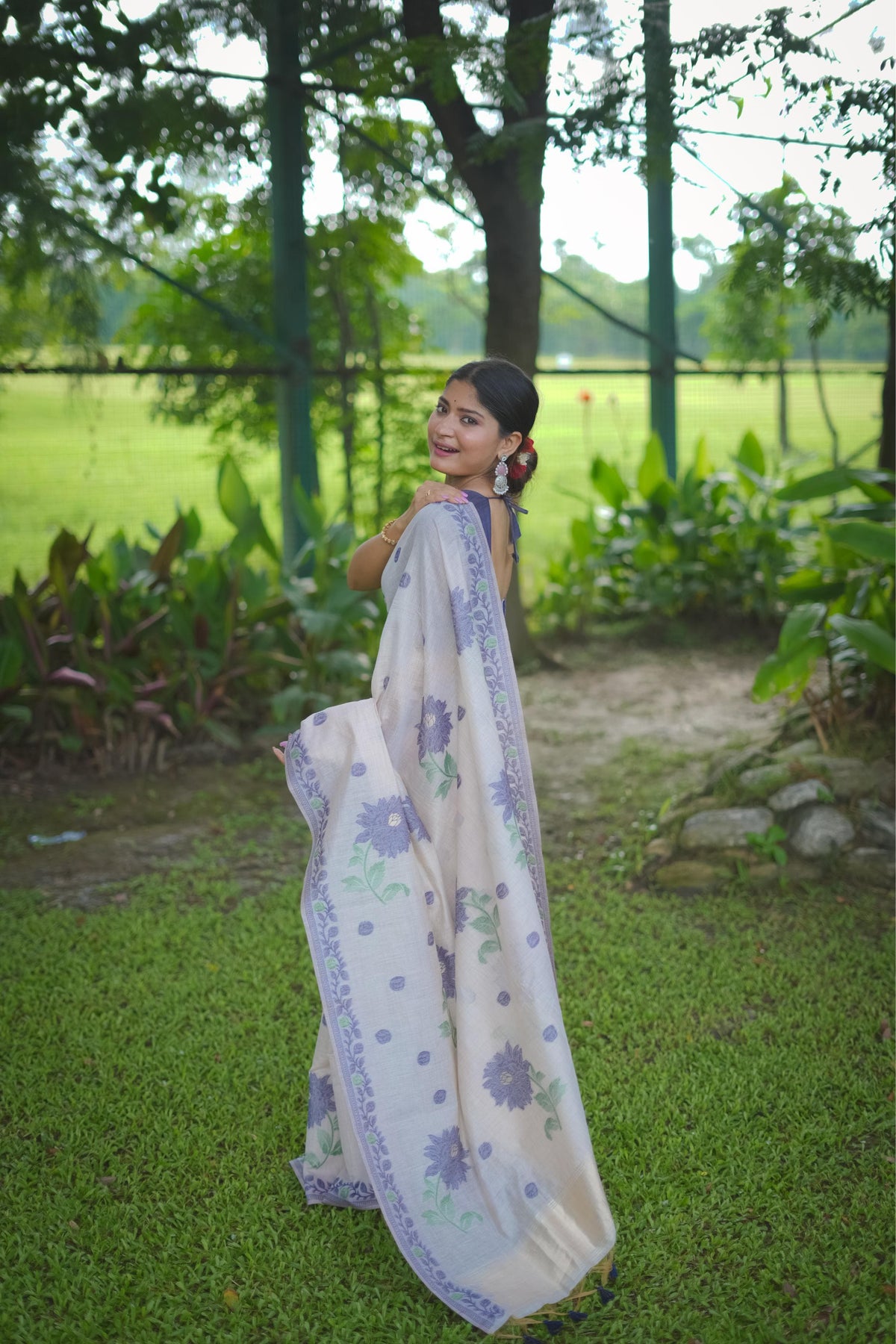 Woman in blue resham weaving saree showcasing back pose with floral design in a garden setting
