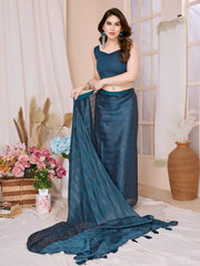 A woman models a chic, sheer Deep Teal Rimzim Silk Saree. The flowing fabric features prominent vertical stripes and scattered embellishments of fine metallic (silver) threadwork. She wears a matching sleeveless teal blouse and accessorizes with bold silver earrings that feature large teal tassels/stones, and stacked silver bangles.