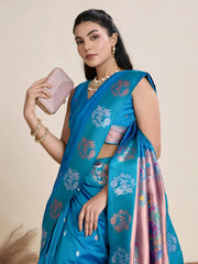 A woman models a luxurious Deep Blue Soft Silk Saree. The saree body features subtle metallic motifs. The pallu features a striking contrast panel in metallic rose gold/copper, richly woven with intricate blue and silver peacock and floral motifs. She wears a matching blue sleeveless blouse and heavy gold Kundan jewelry.