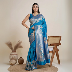 A woman models a luxurious Sea Blue Soft Kanjivaram Silk Saree. The saree features striking large floral and scattered motifs woven in metallic silver Zari on the body and wide pallu. She wears a matching blue sleeveless blouse and accessorizes with a heavy gold Kundan choker necklace and long earrings.
