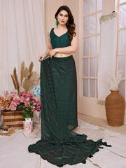 A woman models a chic, sheer Dark Green Rimzim Silk Saree. The flowing fabric features prominent vertical stripes and scattered embellishments of fine metallic (silver) threadwork. She wears a matching sleeveless deep green V-neck blouse and accessorizes with statement gold and green gemstone jewelry, including large earrings.