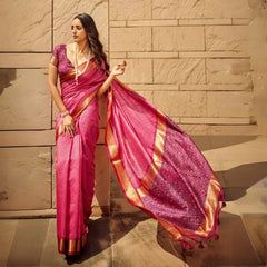 Woman wearing elegant dark pink saree with intricate zari work and patterned pallu standing against stone wall