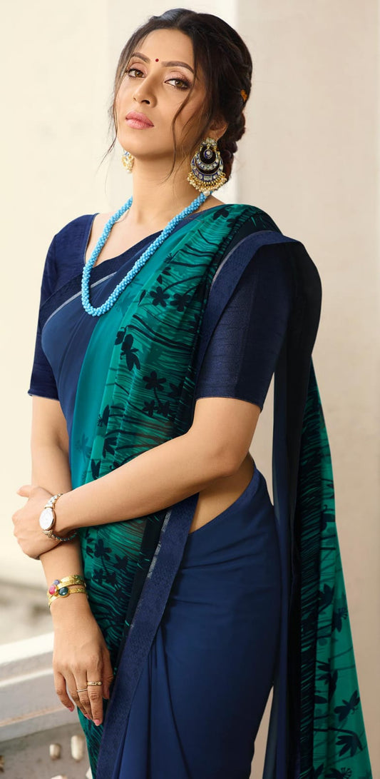 Woman in a dark turquoise jacquard work saree with gold border standing indoors in an elegant room with arched decor and vintage furniture elements