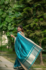 Woman in a dark turquoise saree with zari work posing gracefully on a garden pathway with lush green trees in the background