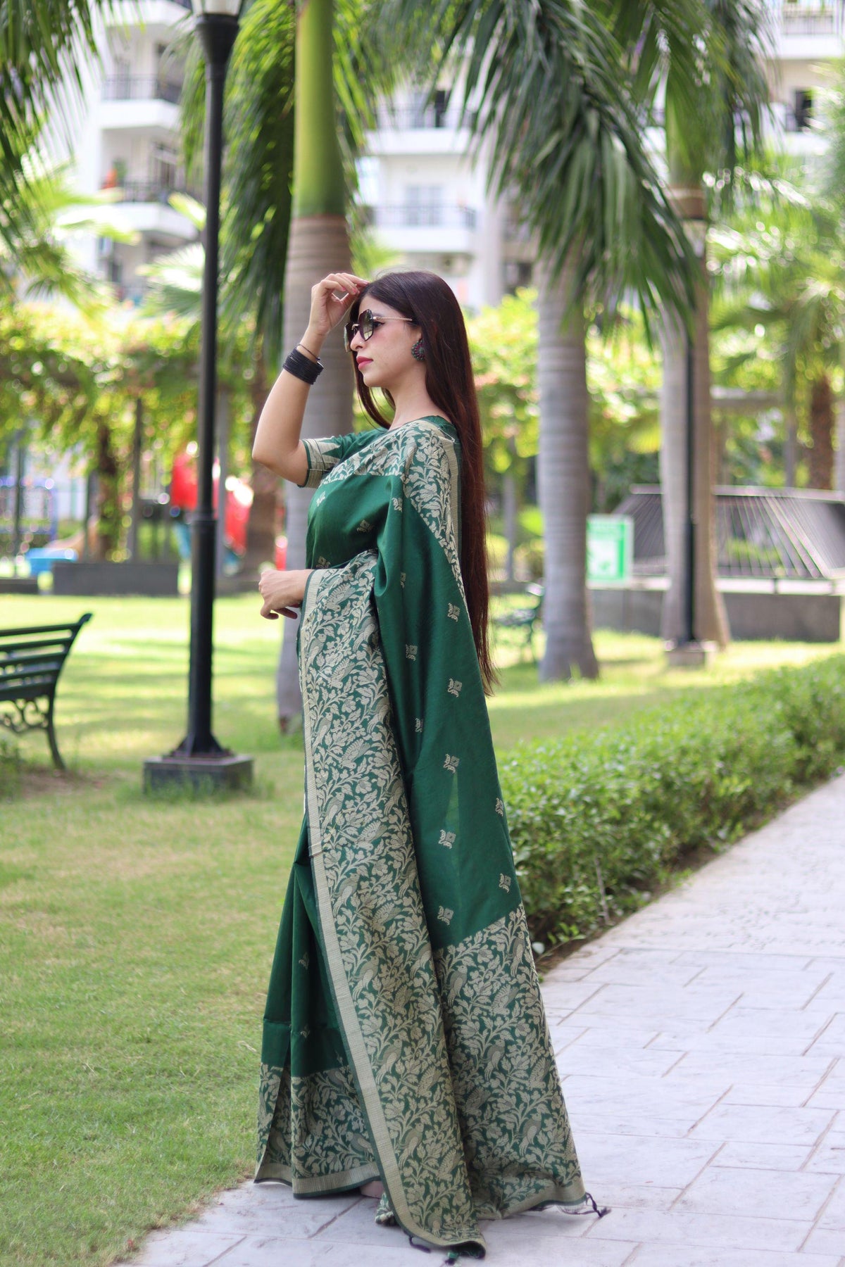  Woman in deep green traditional weaving saree standing elegantly in a garden with palm trees
