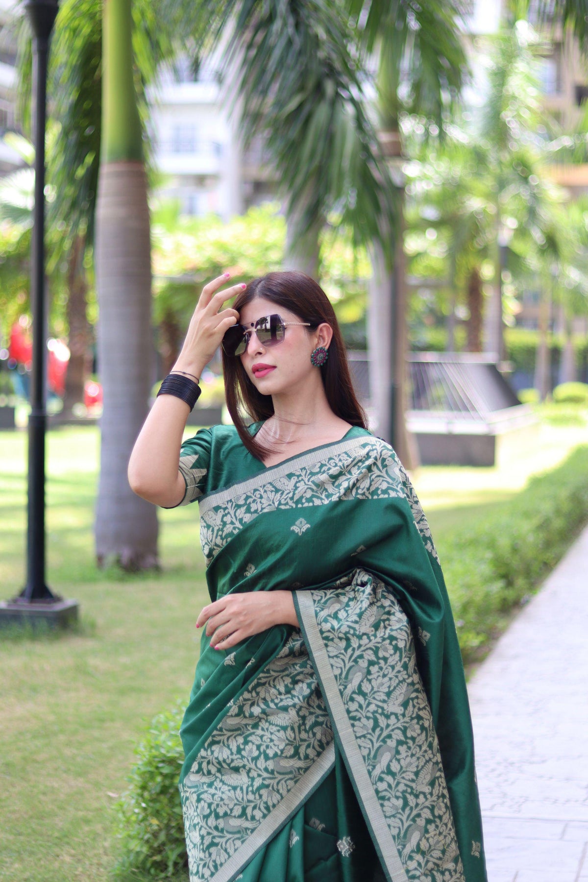  Woman in deep green traditional weaving saree standing elegantly in a garden with palm trees