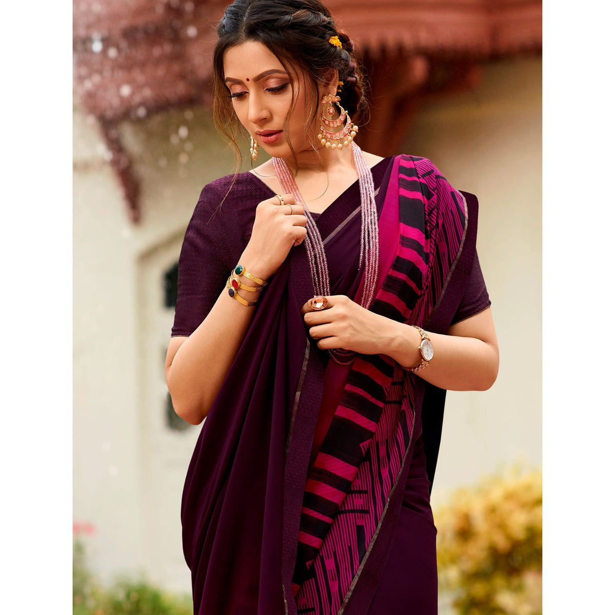 Woman in a deep shade purple jacquard work saree with gold border standing indoors in an elegant room with arched decor and vintage furniture elements