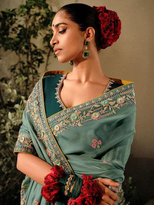 Woman in a dim gray saree with zari work standing near a pond with lotus flowers in a lush garden setting