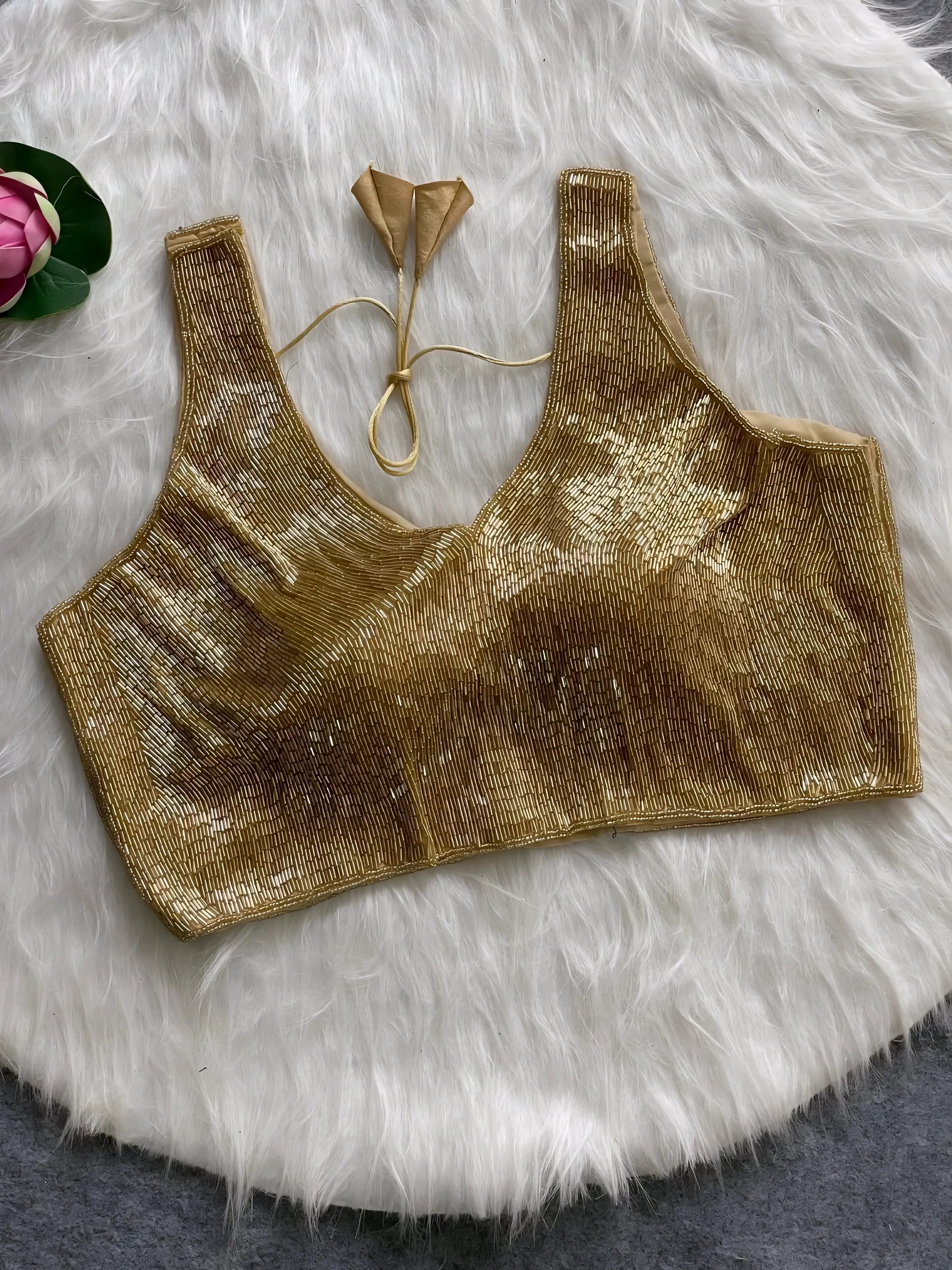 Gold sequin sleeveless blouse with tie-back detail, displayed on a white fur background with a pink floral prop