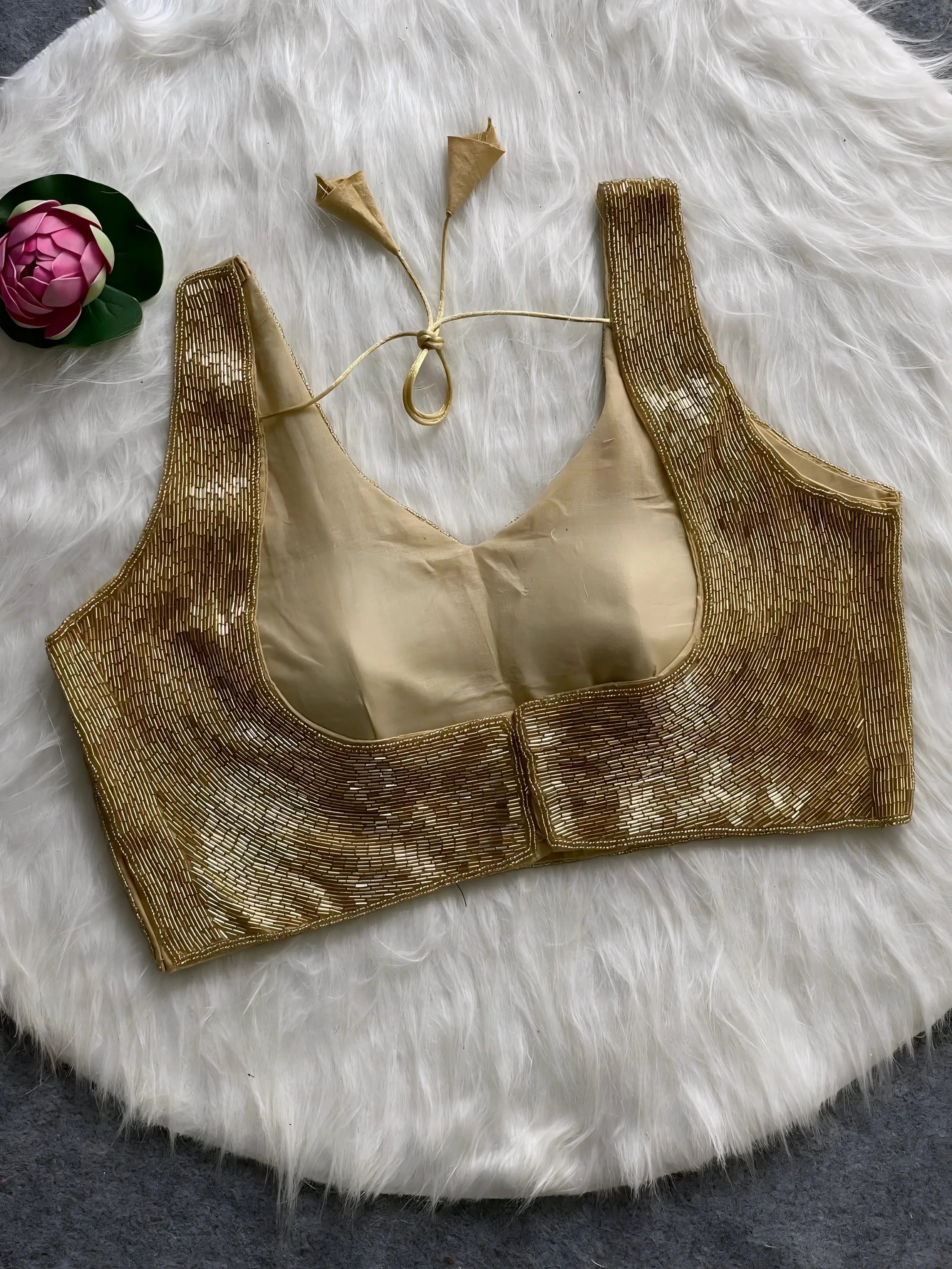 Gold sequin sleeveless blouse with tie-back detail, displayed on a white fur background with a pink floral prop in the corner