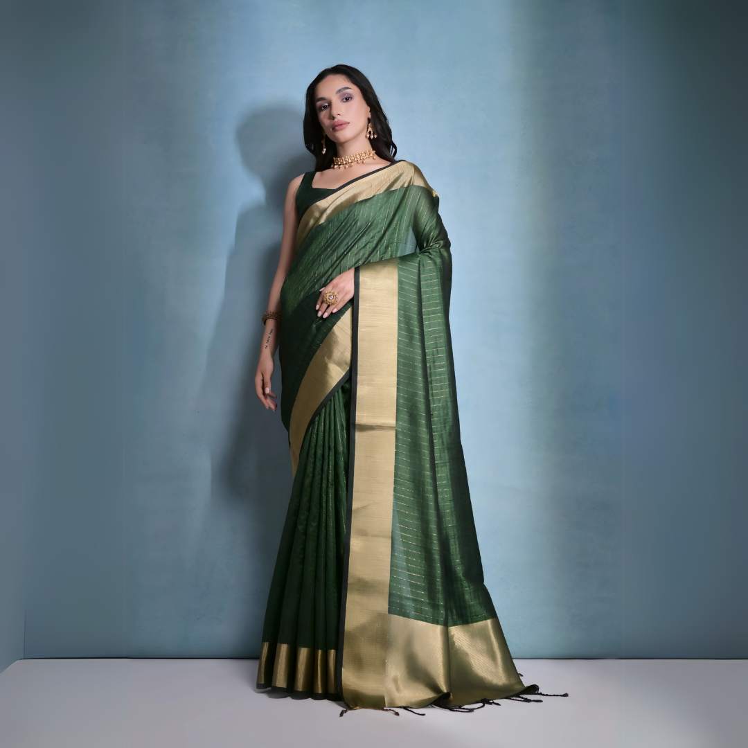 A woman models a striking Dark Green Banarasi Raw Silk Saree. The saree body features subtle gold Zari stripes and is framed by an extremely wide, luxurious metallic gold Zari border. She wears a sleeveless dark blouse and traditional gold Kundan jewelry, posing indoors.