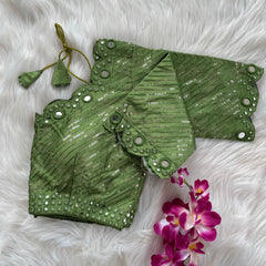 Green bridal blouse with scallop sleeves, featuring silver sequin stripes and mirror work detailing along the neckline, sleeves, and hem, displayed on a textured fur background with a small potted plant nearby.
