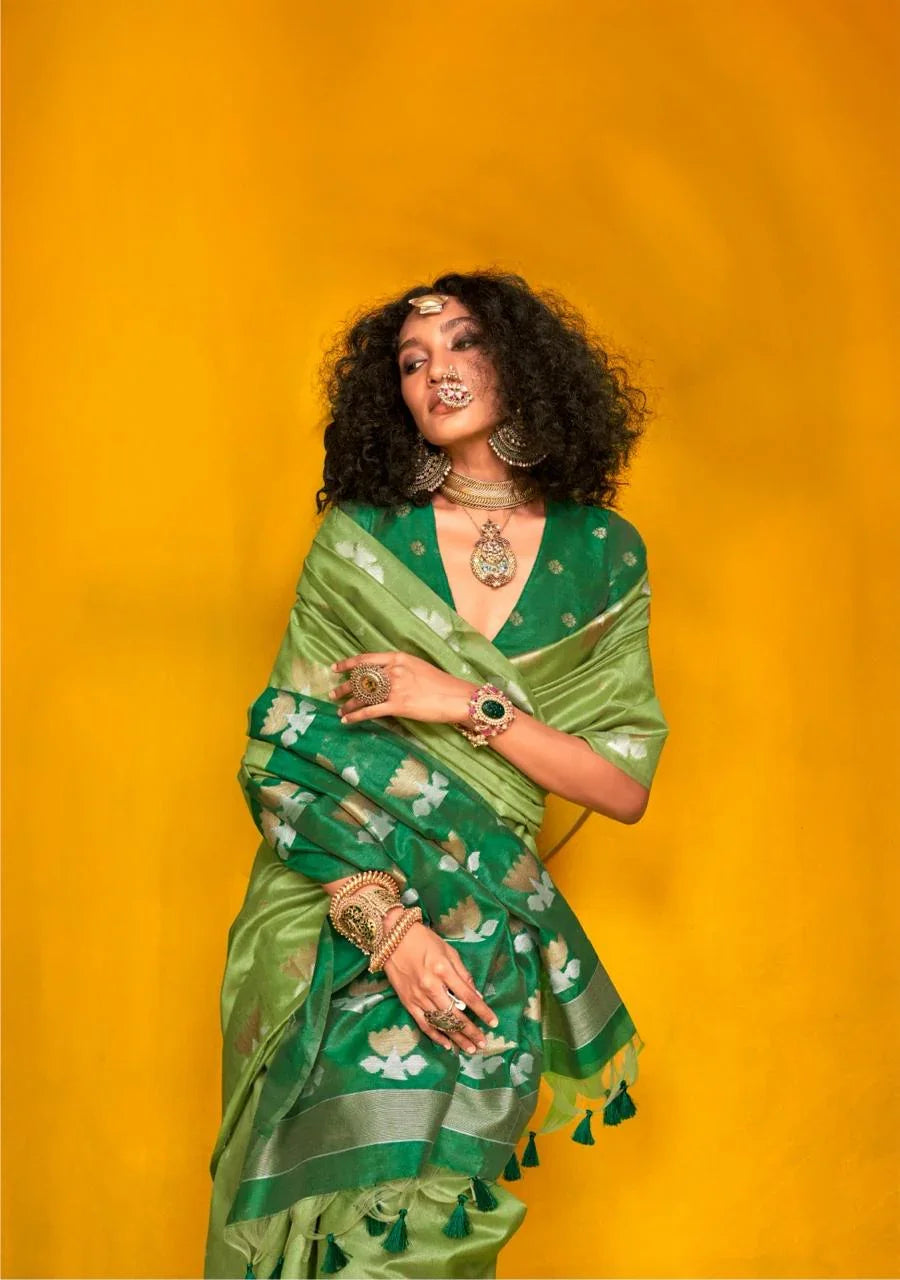 Model in green zari work saree featuring floral motifs and tassels, styled with bold traditional jewellery against a vibrant yellow background