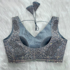  Elegant grey blouse featuring intricate sequin and thread embroidery with floral and leaf motifs, deep V-neck with structured cups, geometric border, and tasseled tie-back detail, displayed flat on a white fur background.