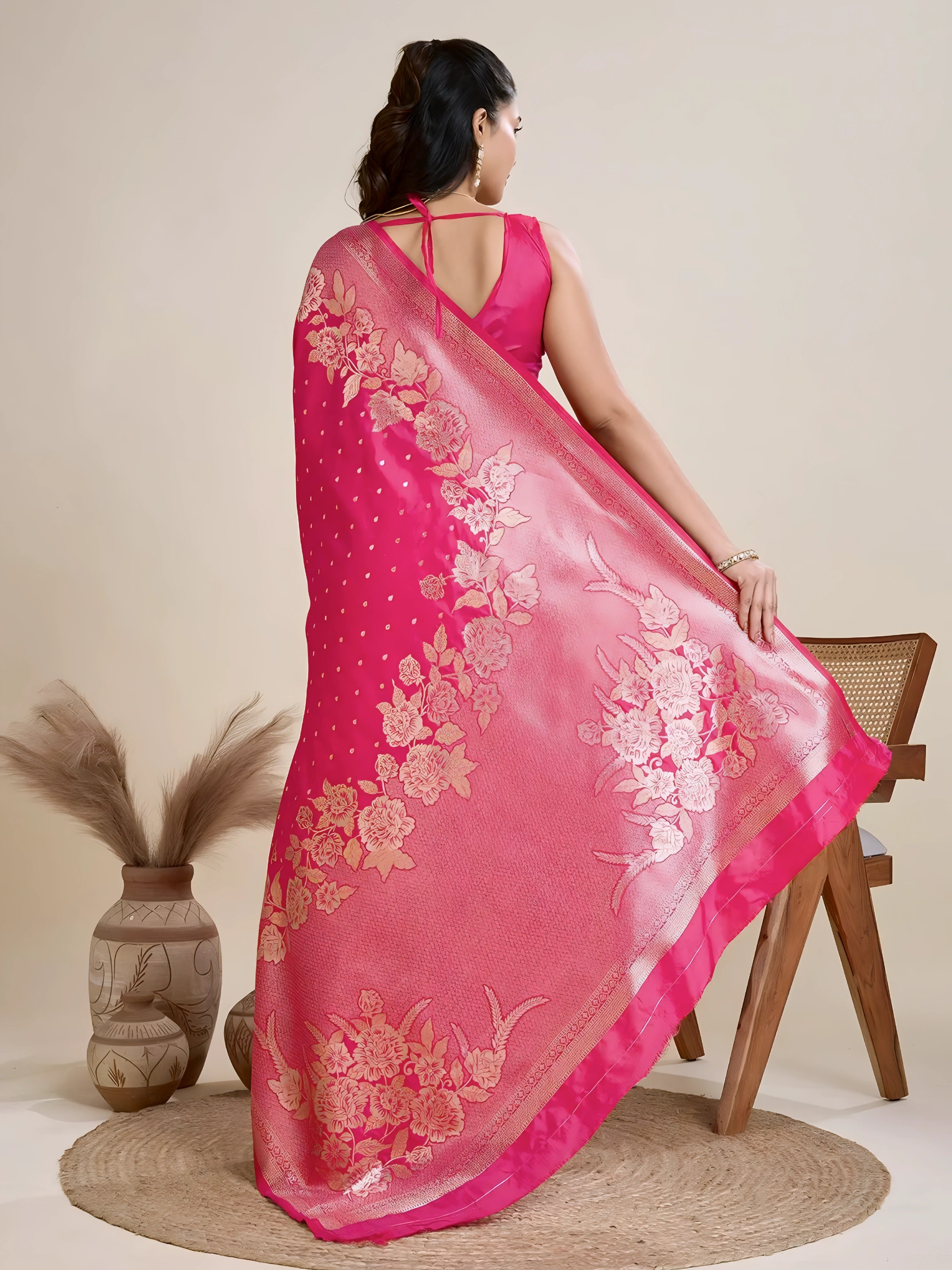 A woman models a luxurious Hot Pink Soft Kanjivaram Silk Saree. The saree features striking large floral and scattered motifs woven in metallic gold Zari on the body and wide pallu. She wears a matching pink sleeveless blouse and accessorizes with a heavy gold Kundan choker necklace and earrings.