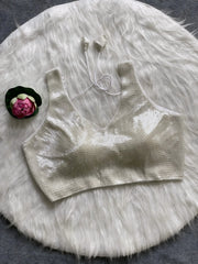 Ivory sequin sleeveless blouse with tie-back detail, displayed on a white fur background with a pink floral prop on the side