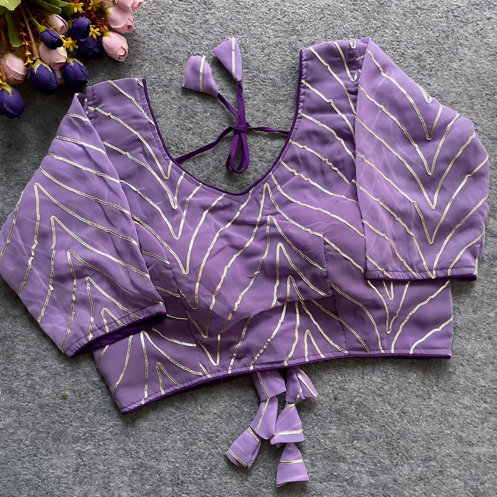 Lavender designer blouse featuring golden thread embroidery, deep back design, and matching fabric tassel tie-up