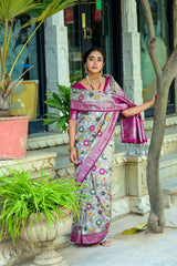 Woman dressed in light gray zari work saree with pink blouse posing gracefully in a traditional Indian setting