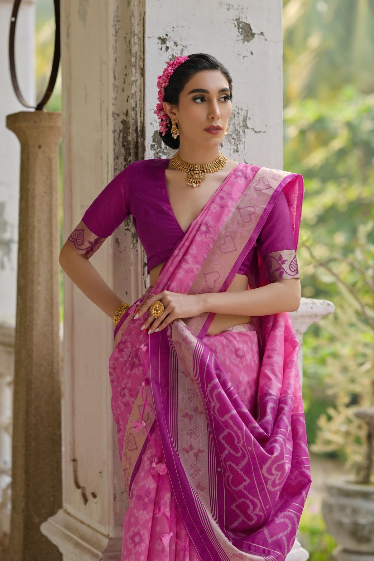 Woman draped in light pink Pochampali Ikkat saree with intricate zari weaving, styled with traditional jewelry in a heritage setting