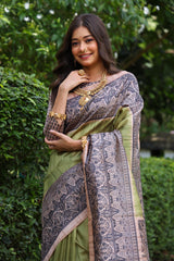 Woman wearing traditional olivine Madhubani print saree with intricate designs and ethnic jewelry in a green outdoor setting