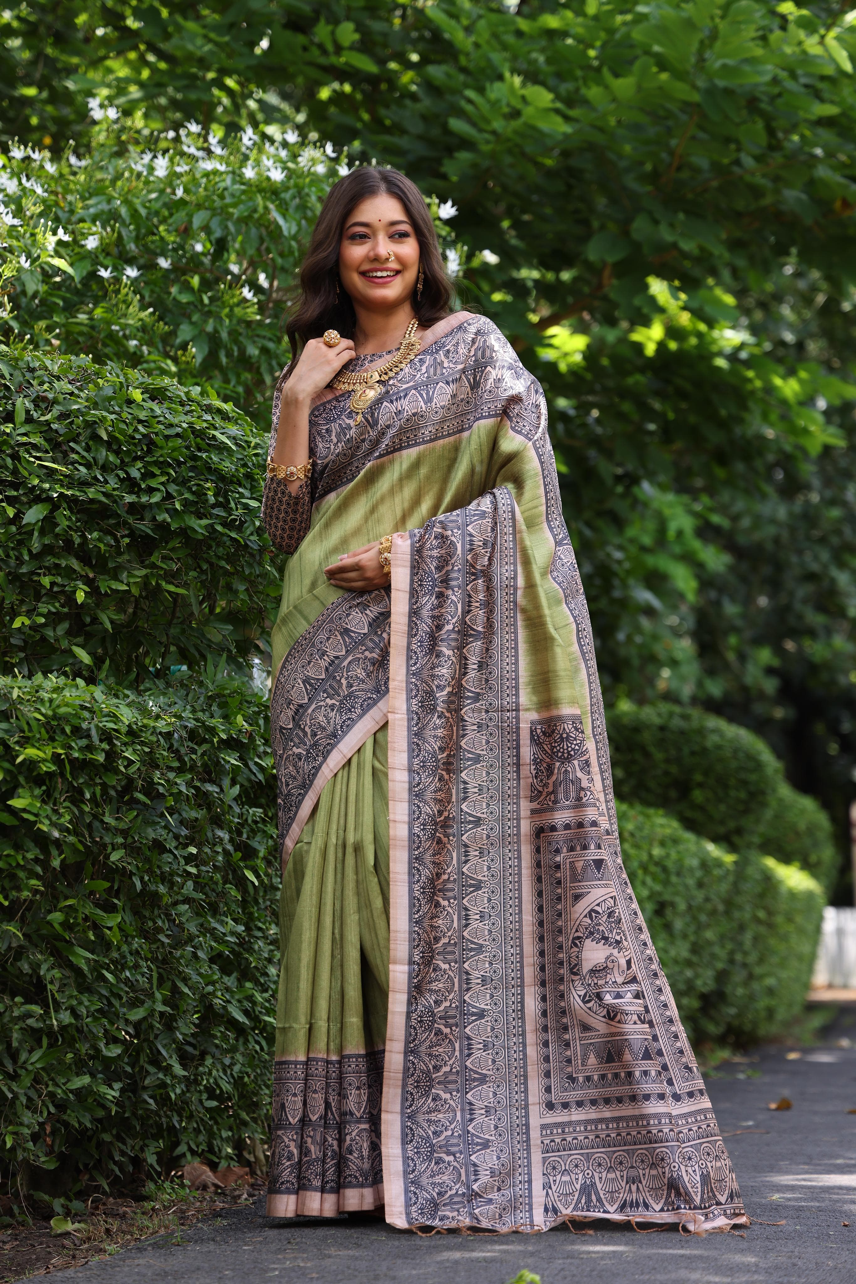 Woman wearing traditional olivine Madhubani print saree with intricate designs and ethnic jewelry in a green outdoor setting
