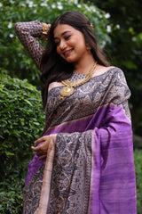 Woman wearing traditional purple Madhubani print saree with intricate designs and ethnic jewelry in a green outdoor setting
