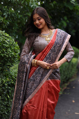 Woman wearing traditional orange Madhubani print saree with intricate designs and ethnic jewelry in a green outdoor setting smiling women