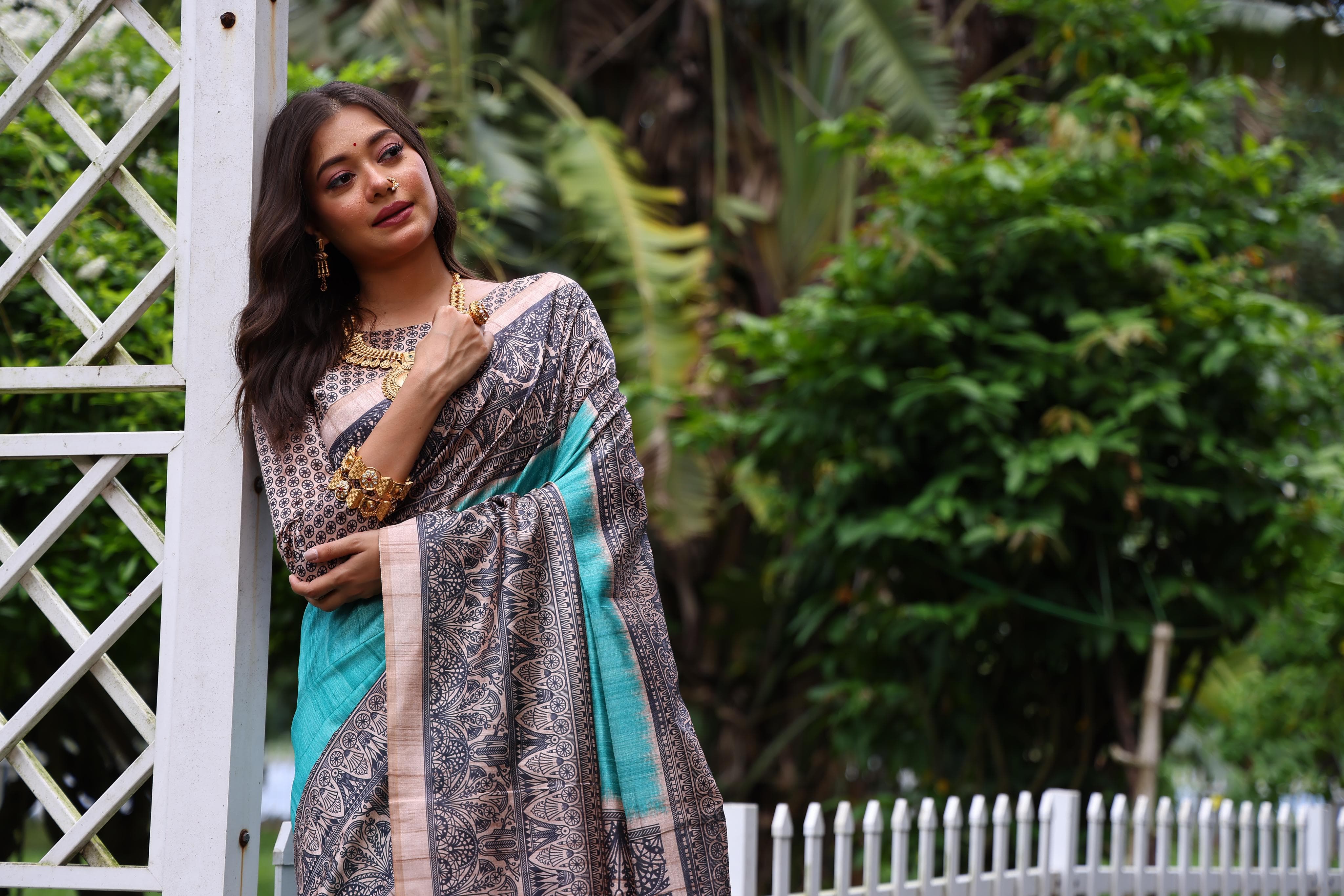 Woman wearing traditional powder blue Madhubani print saree with intricate designs and ethnic jewelry in a green outdoor setting