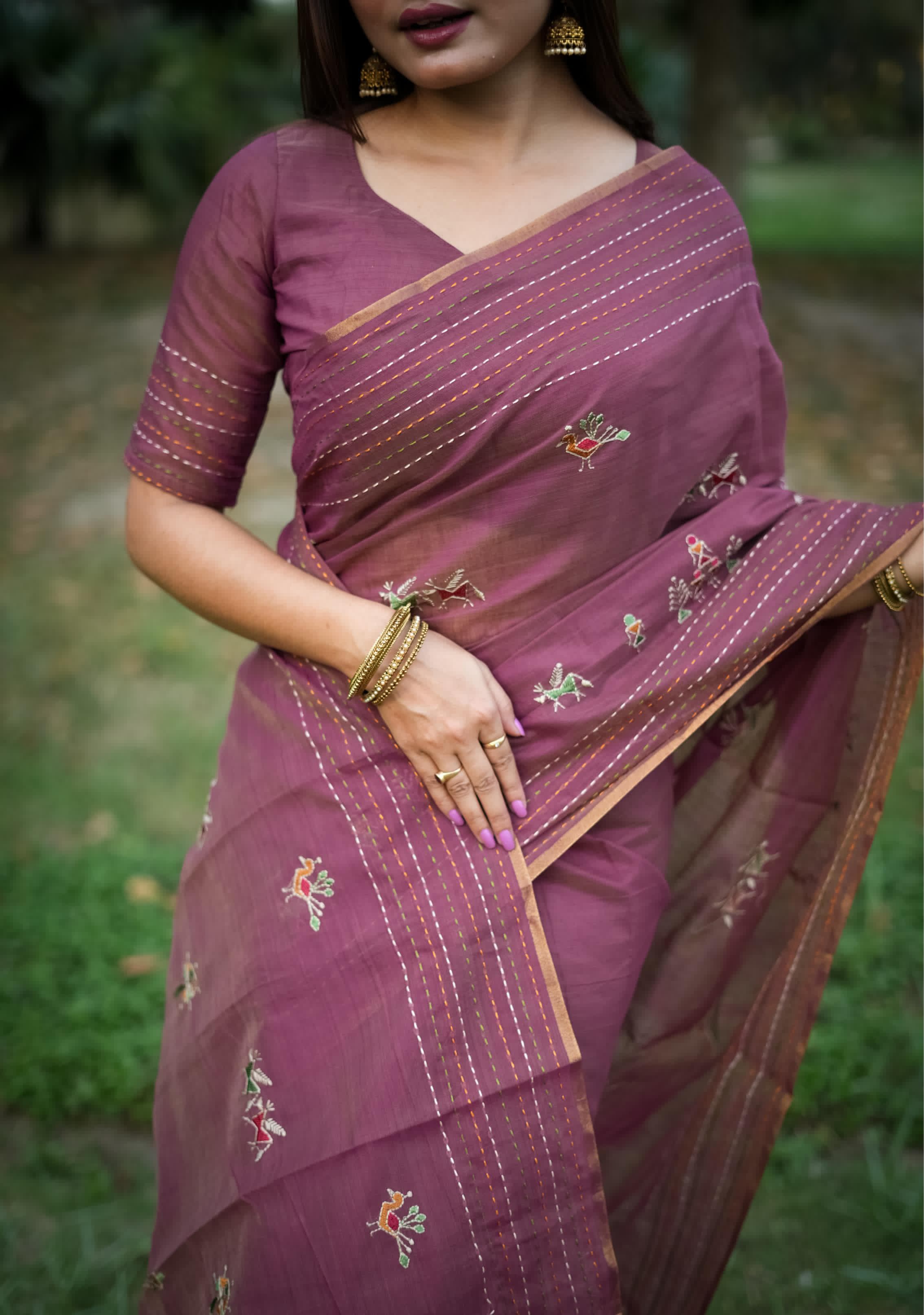 Woman in magenta traditional weaving saree with delicate motifs posing gracefully in a natural outdoor setting.