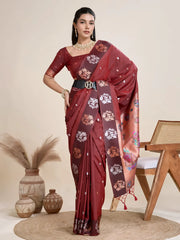 A woman models a luxurious Dark Maroon Soft Silk Saree. The saree features scattered metallic motifs and a wide, contrasting peach/copper pallu panel richly woven with multi-colored traditional figurative and floral designs. She wears a matching brown blouse and heavy gold Kundan jewelry, posing indoors.