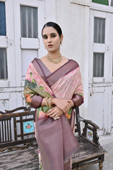 A woman models an elegant Light Peach Soft Silk Saree featuring a large-scale floral and figurative Pichwai-style print in soft colors. The saree has a wide Deep Brown/Maroon border and pallu. She wears a matching dark blouse and a gold Kundan choker necklace, posing outdoors next to distressed antique white doors.