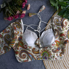 Multicolor paisley embroidered padded blouse with tie-up detail, displayed on a grey surface with artificial pink flowers and green leaves in the background
