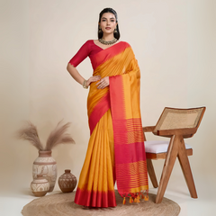 A woman models a striking Mustard Yellow Raw Silk Saree. The pallu and border contrast dramatically in a wide band of vibrant Red/Fuchsia Pink with traditional temple and horizontal stripe weaving. She wears a red short-sleeve blouse and accessorizes with a chunky dark gemstone necklace, posing indoors.