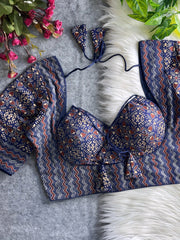 Navy and maroon printed padded blouse with geometric and floral patterns, displayed on a white fur surface with artificial flowers and green leaves in the background.