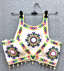 Off-white blouse featuring vibrant circular and oval mirror work with traditional Kutch multicolor embroidery, accented by geometric borders and shell tassel drops along the hem. Displayed on a hanger against a textured silver background, highlighting its festive and culturally inspired ethnic design.