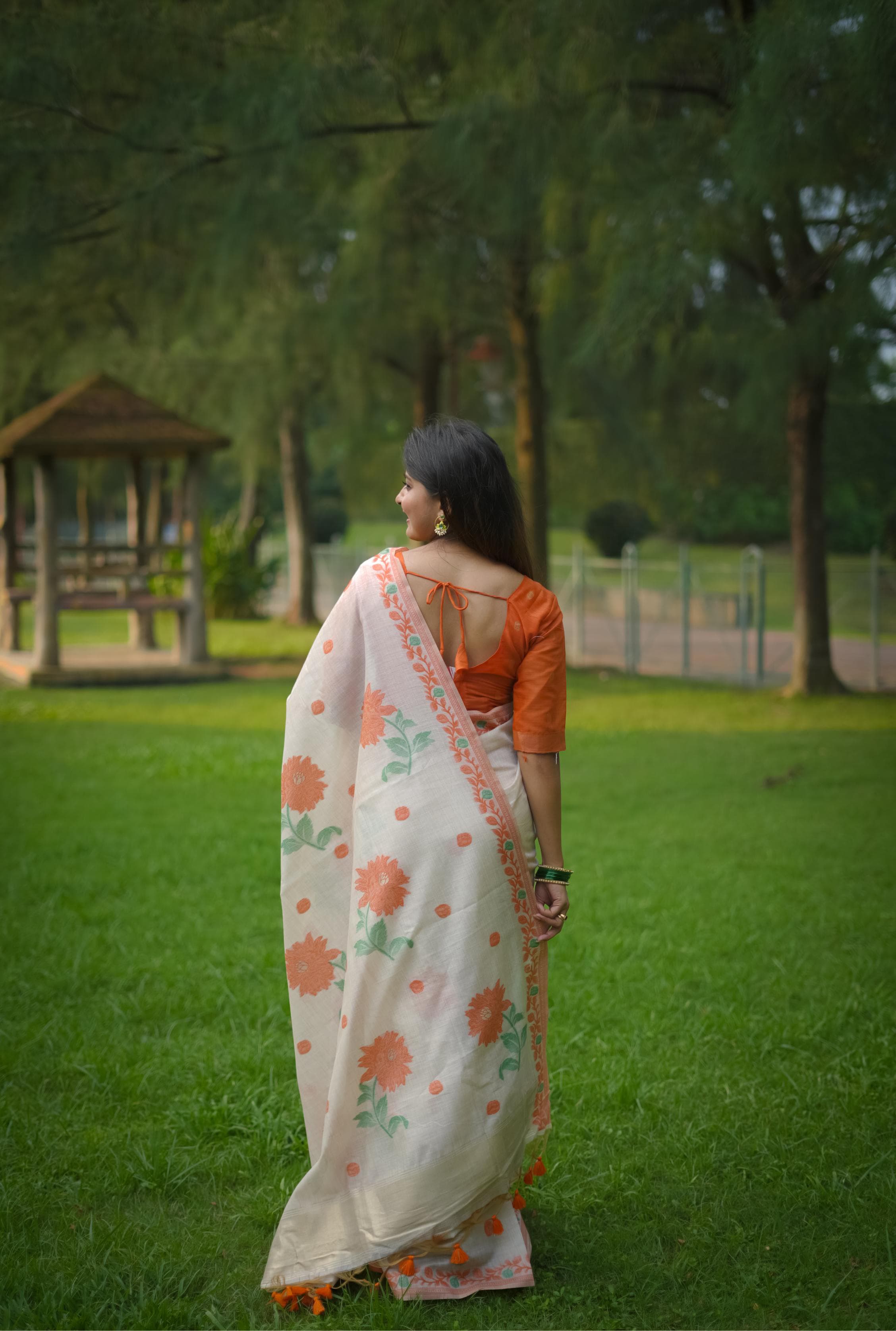 Back view of woman wearing orange resham weaving saree with floral motifs in garden setting