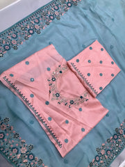 A woman models an ethereal Light Sea Blue Silk Saree. The saree features a wide, heavy border and pallu of intricate floral and vine embroidery in soft pink, teal, and silver threadwork. She wears a contrasting short-sleeve soft pink embroidered blouse and accessorizes with delicate silver/diamond jewelry, posing indoors.