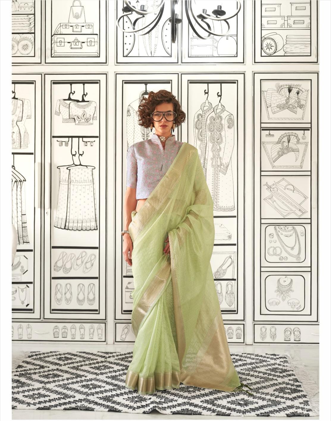 Woman in a pastel pistachio green saree with zari work standing against a fashion-themed illustrated background