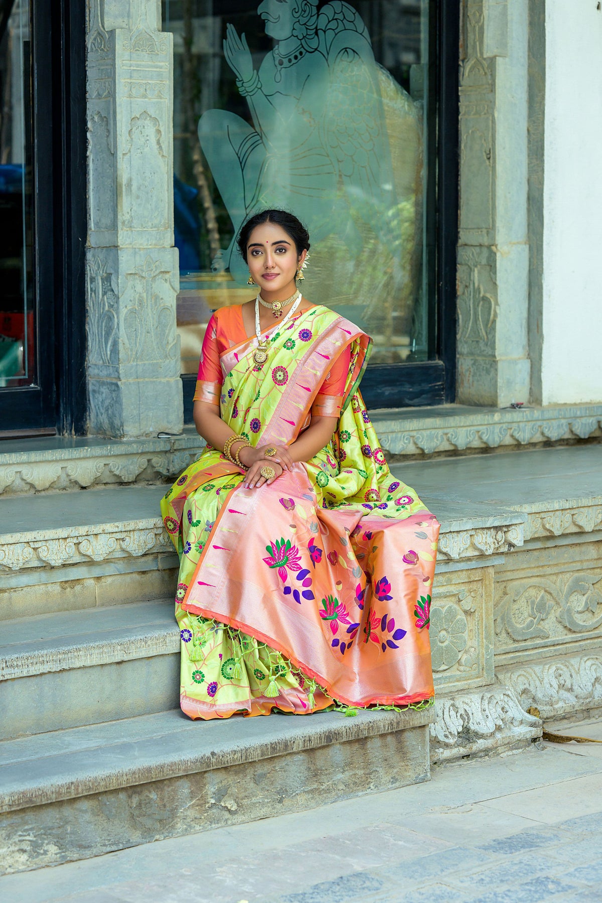 Woman seated in pastel pistachio green zari work saree with peach border and blouse, showcasing traditional Indian attire