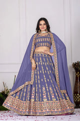 Woman wearing a traditional purple and gold embroidered outfit with a matching dupatta against a white wall.