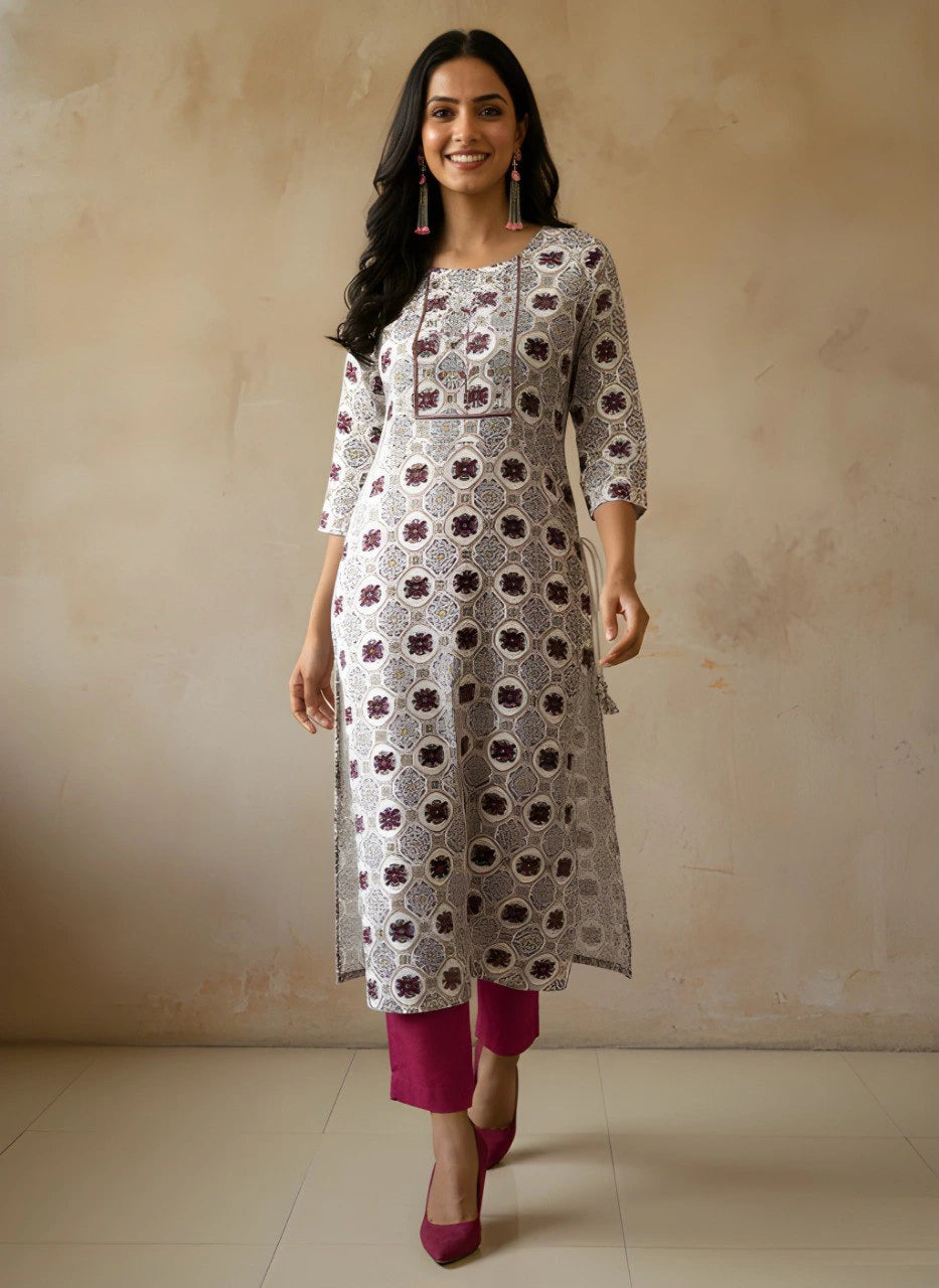 Woman wearing a patterned kurta with pink pants against a beige wall.