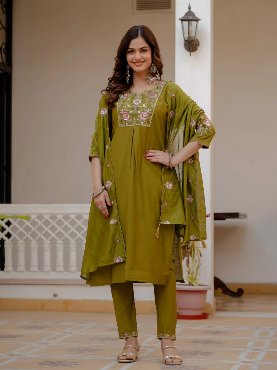 Woman wearing a green traditional outfit with floral embroidery indoors.