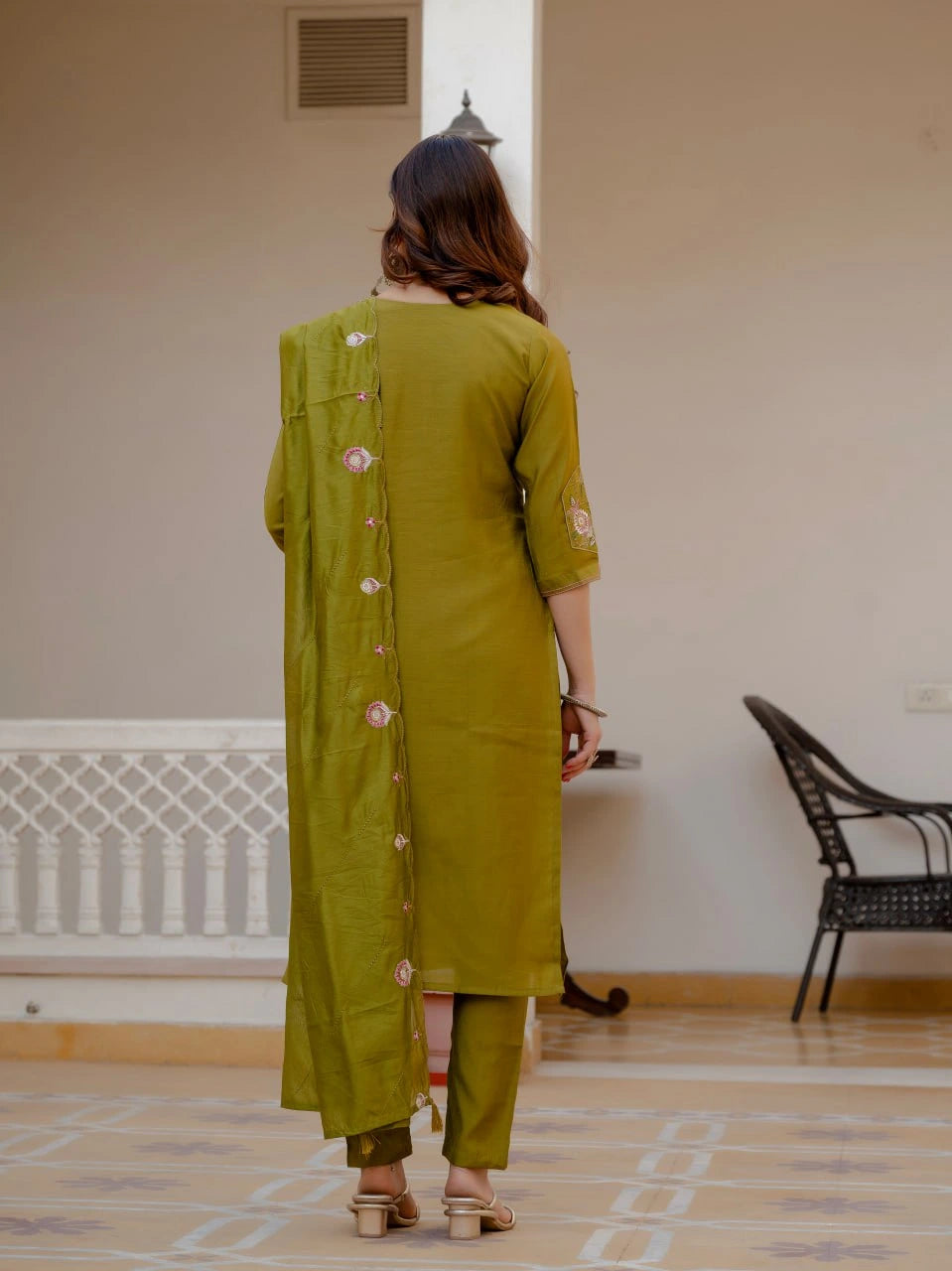 Woman wearing a green traditional outfit in a room with a chair and radiator.