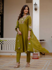 Woman wearing a green embroidered outfit standing in a room with a neutral background.